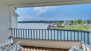 Een balkon met witte stoelen en uitzicht op een jachthaven met boten en gebouwen.