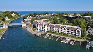 An aerial view of a waterfront hotel with a swimming pool, docked boats, and a bridge connecting to the mainland. - Edgewater 357 | Downtown Charlevoix | Pool, Hot Tub, Sauna (Charlevoix)