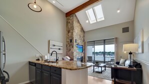 A modern kitchen with a stone accent wall, a dining area with a view, and a cozy seating area. - Edgewater 357 | Downtown Charlevoix | Pool, Hot Tub, Sauna (Charlevoix)