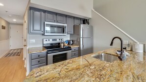 A modern kitchen with grey cabinets, a stainless steel refrigerator, a microwave, and a granite countertop. - Edgewater 357 | Downtown Charlevoix | Pool, Hot Tub, Sauna (Charlevoix)