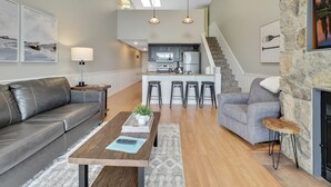 A modern living room with a leather sofa, a wooden coffee table, and a stone fireplace. - Edgewater 357 | Downtown Charlevoix | Pool, Hot Tub, Sauna (Charlevoix)