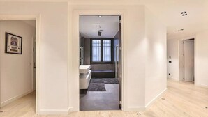 A hallway leading to a bathroom with a window, a framed picture on the wall, and a door on the right. - YOUR SOLUTION TO A LUXURY STAY- 250M2 TOP LUXURY CHAMPS ELYSEES (Paris)
