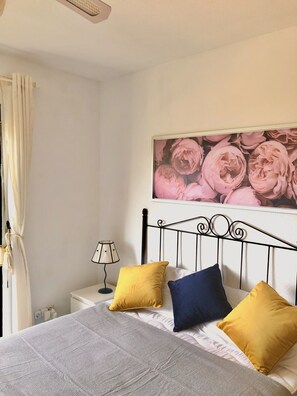 Um quarto com uma cama, uma mesa de cabeceira, uma luminária e uma parede com um quadro floral.