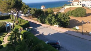 A residential area with a road, parked cars, and houses with ocean views.
