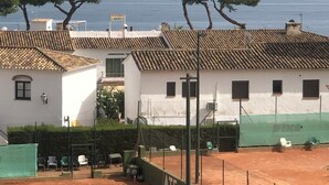 A residential area with white buildings, a tennis court, and a view of the sea.