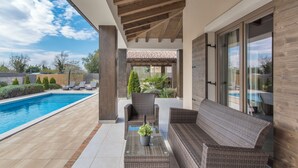 A covered outdoor area with a pool, wicker furniture, and a potted plant.