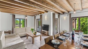 A spacious living area with a wooden ceiling, a sofa, a TV, and a dining table set for a meal.