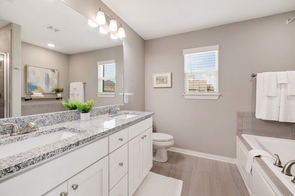 A modern bathroom with a granite countertop sink, a toilet, and a bathtub.