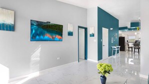 A modern interior with a large flat-screen TV, a vase with flowers, and a kitchen area in the background. - Fortune Rise. Car Rental available  (Mount Fortune)