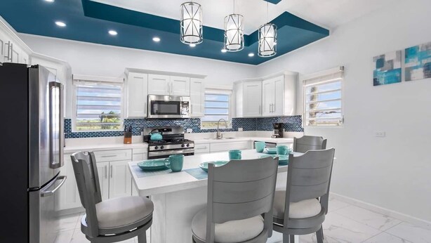 A modern kitchen with white cabinets, a central island with seating, stainless steel appliances, and blue-tiled backsplash. - Fortune Rise. Car Rental available  (Mount Fortune)