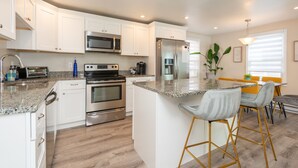A modern kitchen with white cabinets, stainless steel appliances, and a central island with bar stools. - 3 bedroom condo nestled in Historic fishing village - dog friendly (Swampscott)