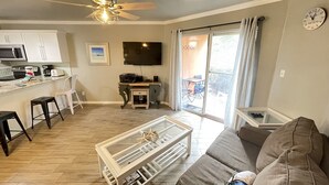 Un salon moderne avec un canapé, une table basse et un téléviseur. Il y a également un coin cuisine avec des placards et des appareils électroménagers.