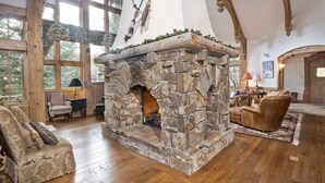 A stone fireplace with a rustic design, surrounded by wooden beams and large windows. - 349 Holden Rd. 5 Bedroom Home by RedAwning (Avon)