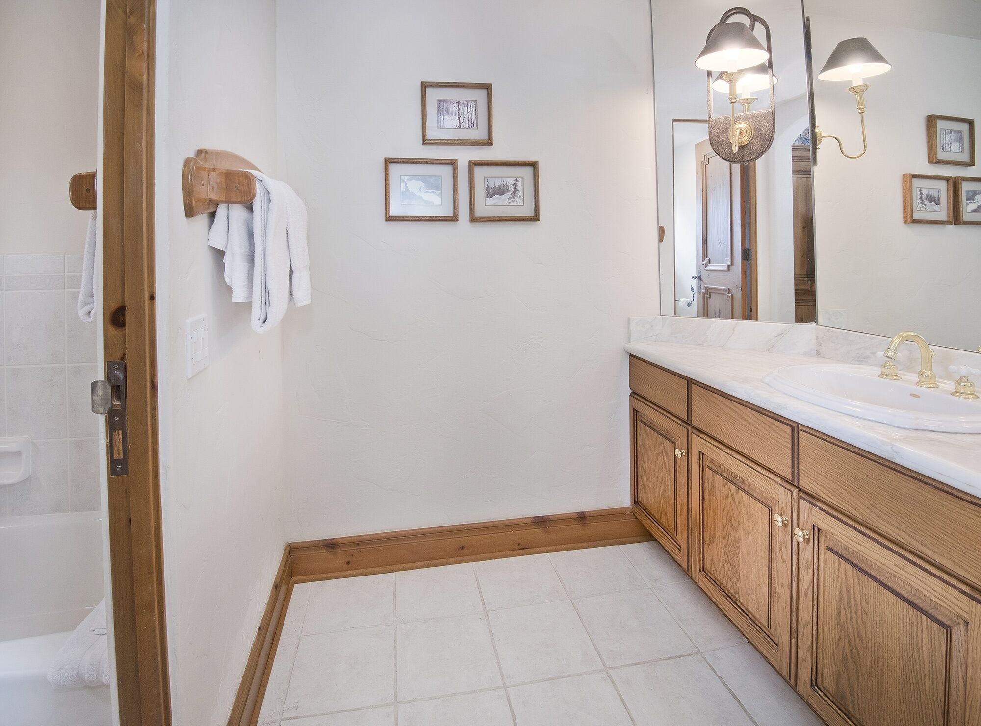 A bathroom with a wooden vanity, a large mirror, and framed pictures on the wall.