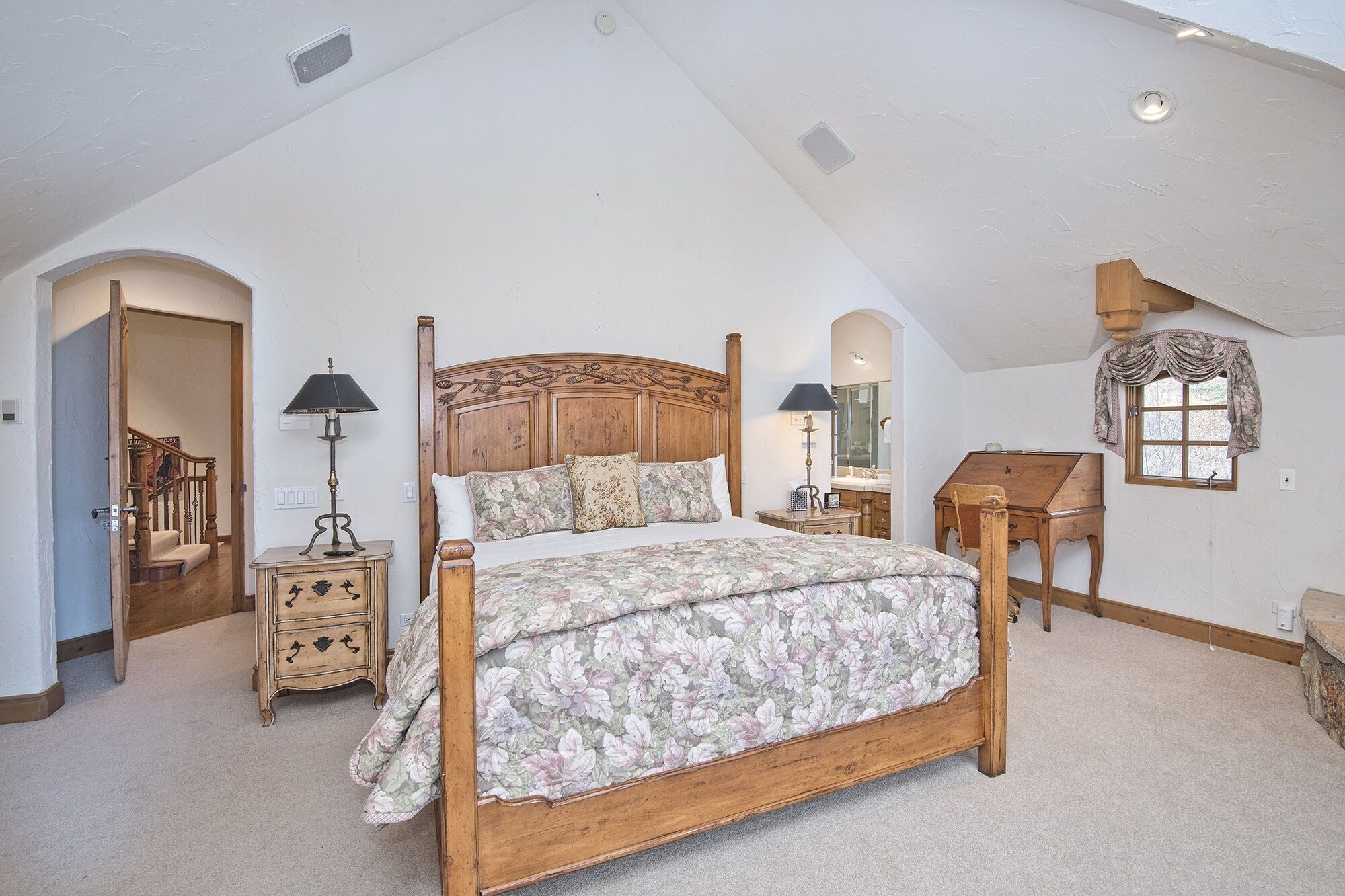 A bedroom with a large bed, two bedside tables, a wooden desk, and a mirror.