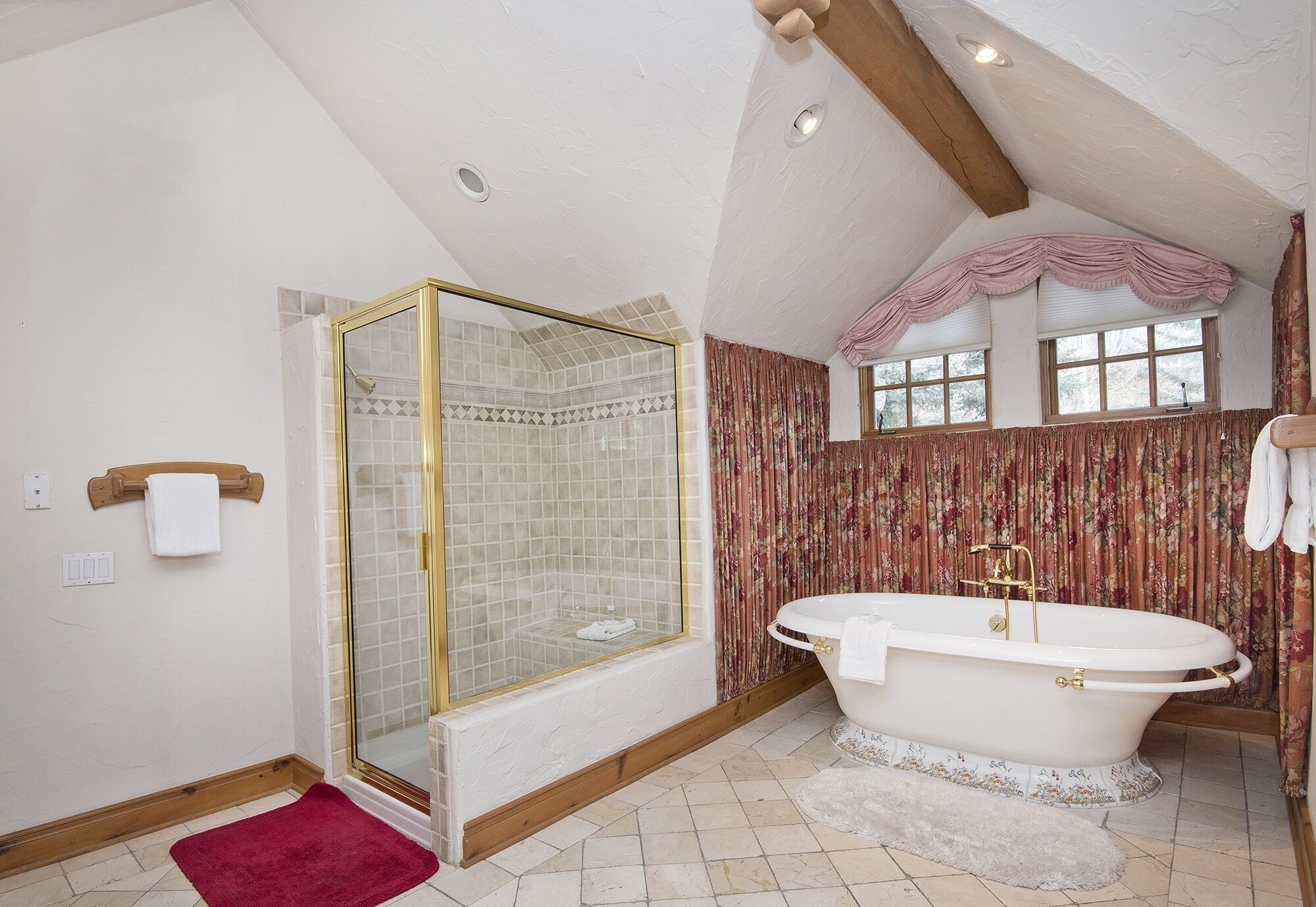A bathroom with a glass-enclosed shower, a freestanding bathtub, and a window with curtains.