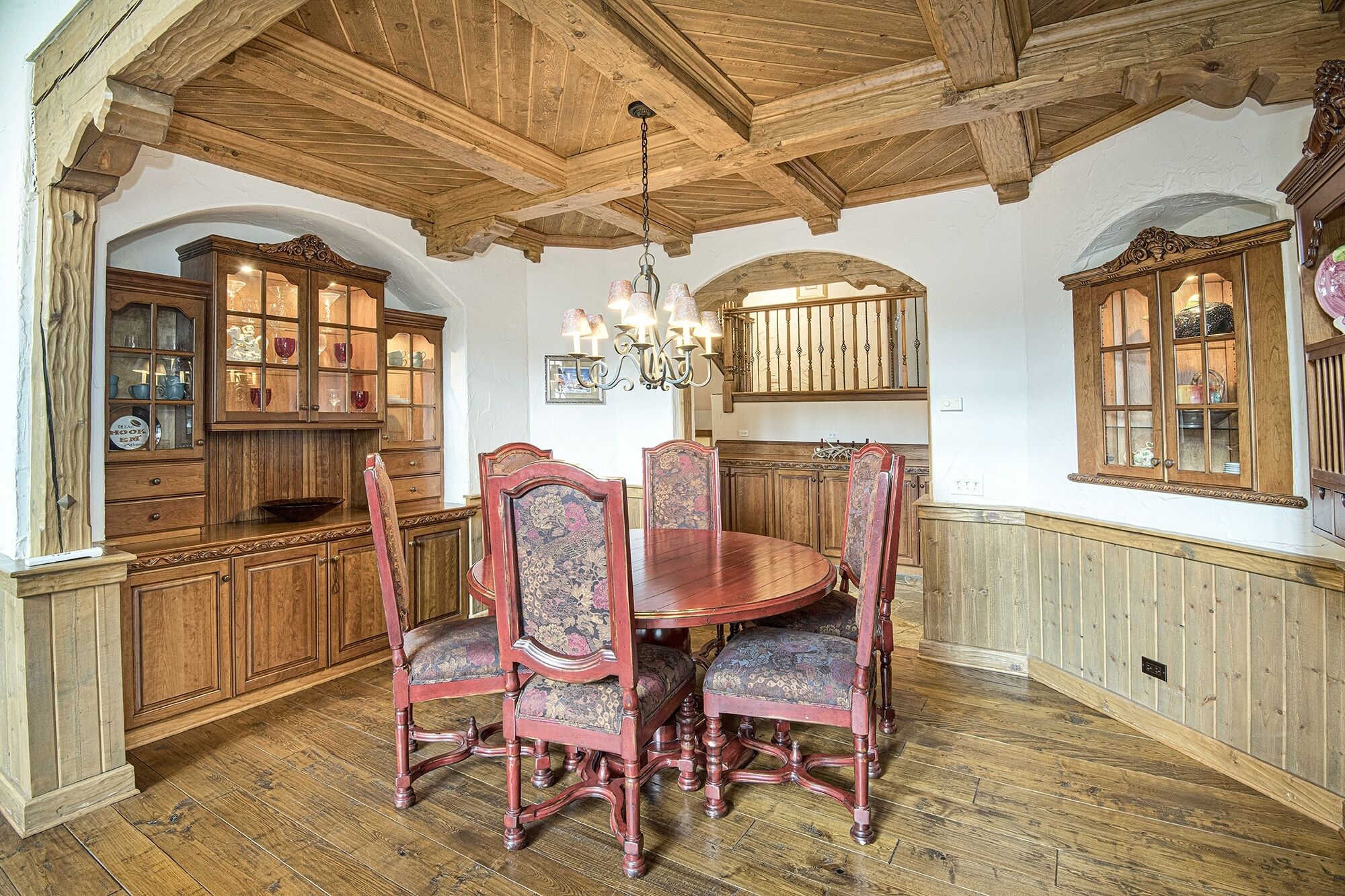 A dining area with a wooden table and chairs, a chandelier, and wooden cabinets with glass doors.