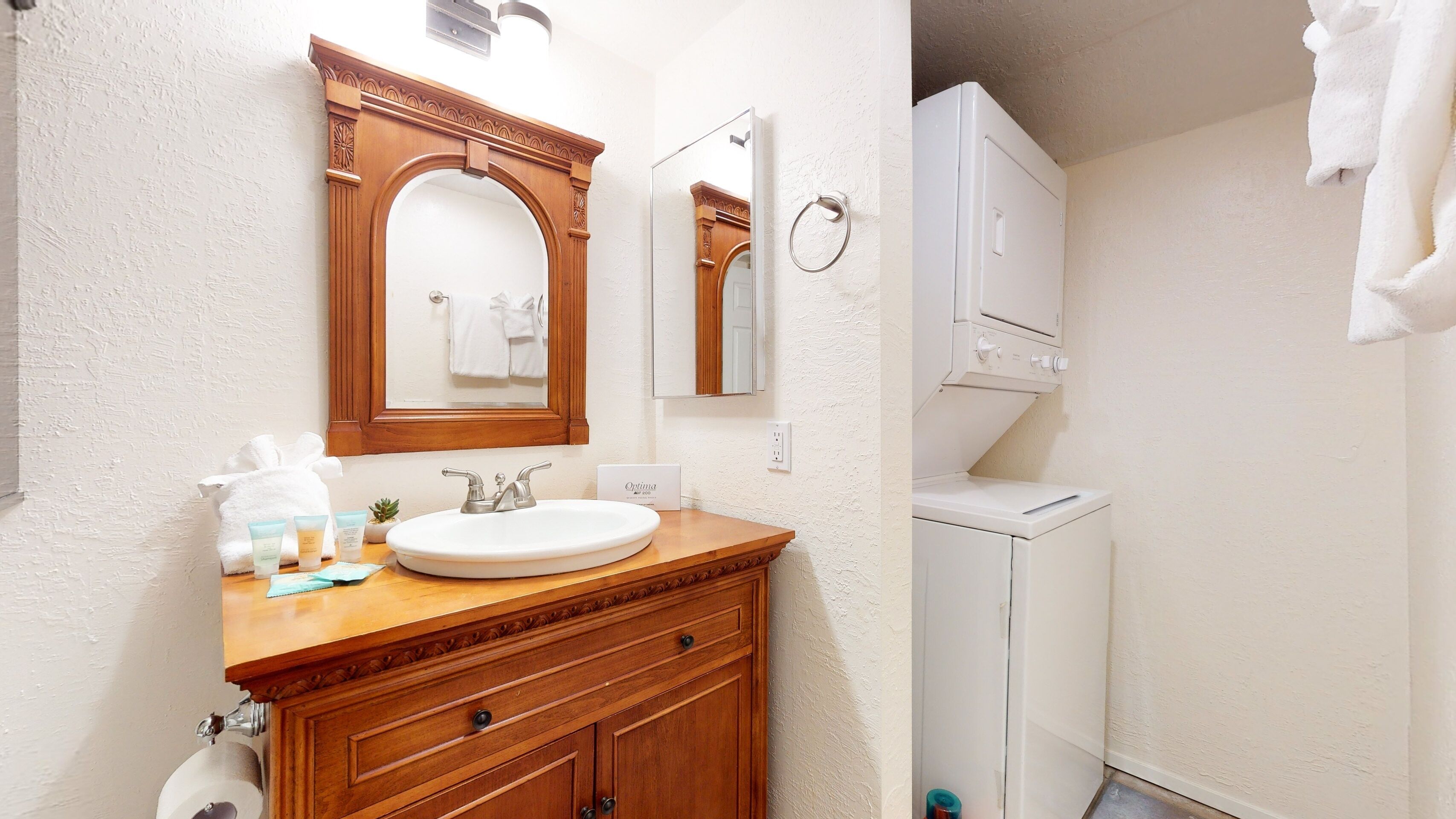 A bathroom with a wooden vanity, a sink, a mirror, a towel rack, and a washing machine.