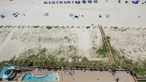 An aerial view of a beach resort with a swimming pool, beach umbrellas, and lounge chairs.