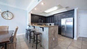 A modern kitchen with dark cabinets, a stainless steel refrigerator, and a bar area with stools.