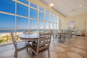 A dining area with large windows overlooking a beach, featuring round tables and chairs.