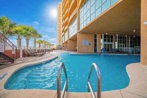 A swimming pool with a sunshade, lounge chairs, and a building with large windows.