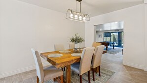 Un coin repas comprenant une table en bois, six chaises, un lustre et un vase avec des fleurs.