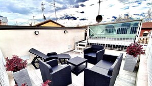 Area patio esterna con mobili in rattan, tra cui divani e un tavolo, e piante in vaso.