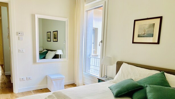 Cama bem arrumada com travesseiros verdes, luminária de cabeceira e um quadro na parede.