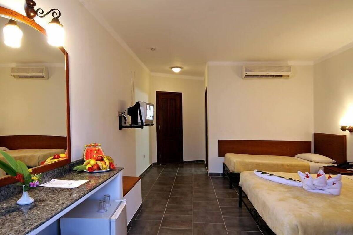 A hotel room with two beds, a small kitchenette, a mirror, and a television.
