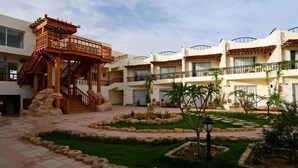 Un patio con un pabellón de madera tradicional, un edificio de varios pisos con balcones y una zona de jardín bien cuidada.