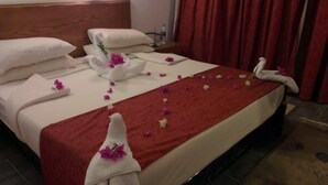 Habitación de hotel con una cama bien hecha, una manta roja y toallas con motivos florales.