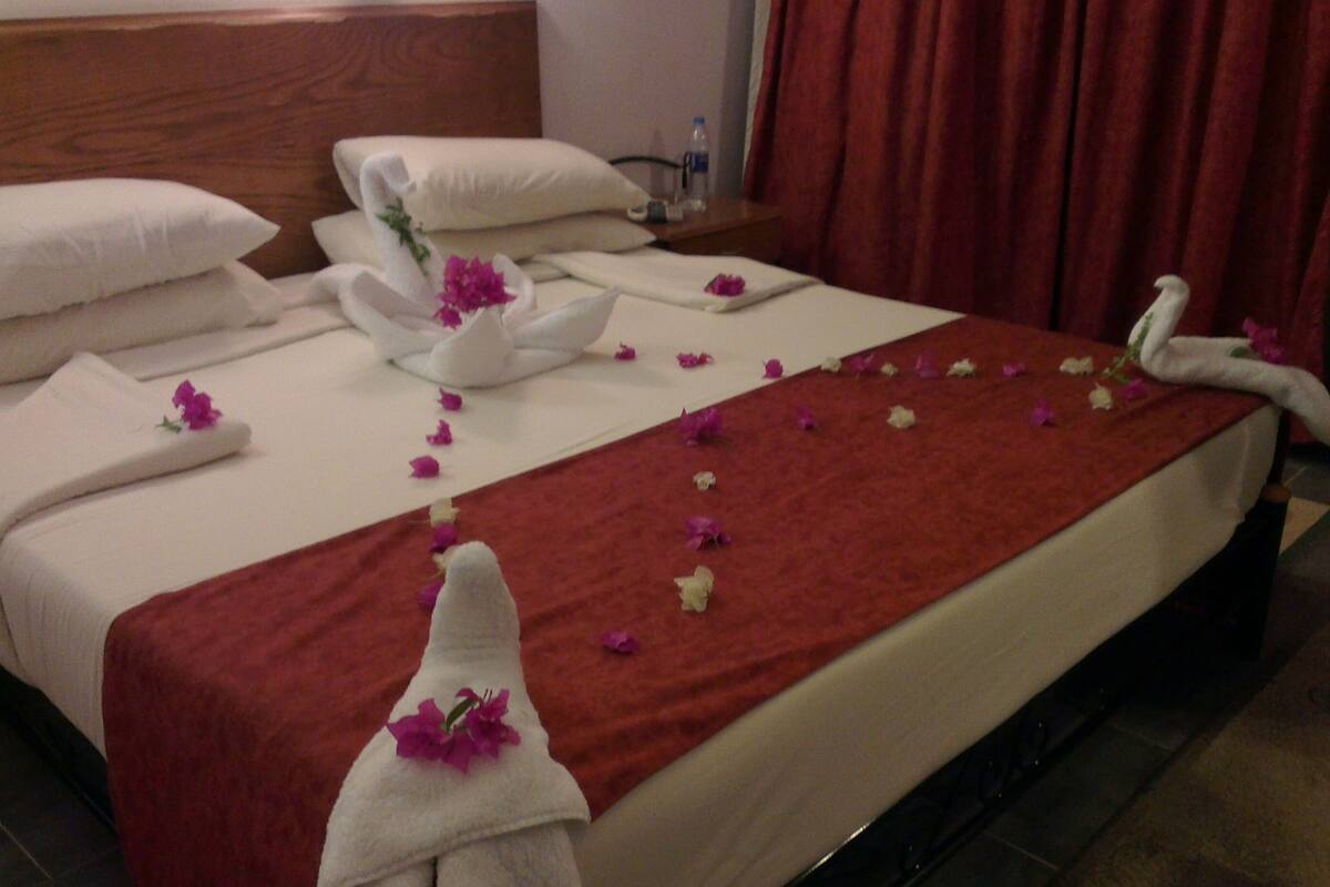 A hotel room with a neatly made bed, a red throw blanket, and towels with flowers.