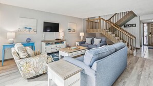 Una sala de estar moderna con una escalera, un sofá, una mesa de centro y un televisor montado en la pared.