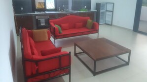 A modern living room with two red sofas, a wooden coffee table, and a kitchen area with a refrigerator and a microwave.