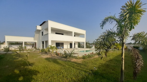 A modern two-story house with a swimming pool, surrounded by greenery and palm trees.