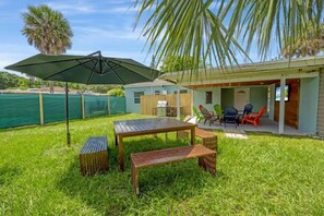 Ein Garten mit einem Holztisch und einer Bank, eine Terrasse mit Stühlen und ein überdachter Bereich mit Tisch und Stühlen.
