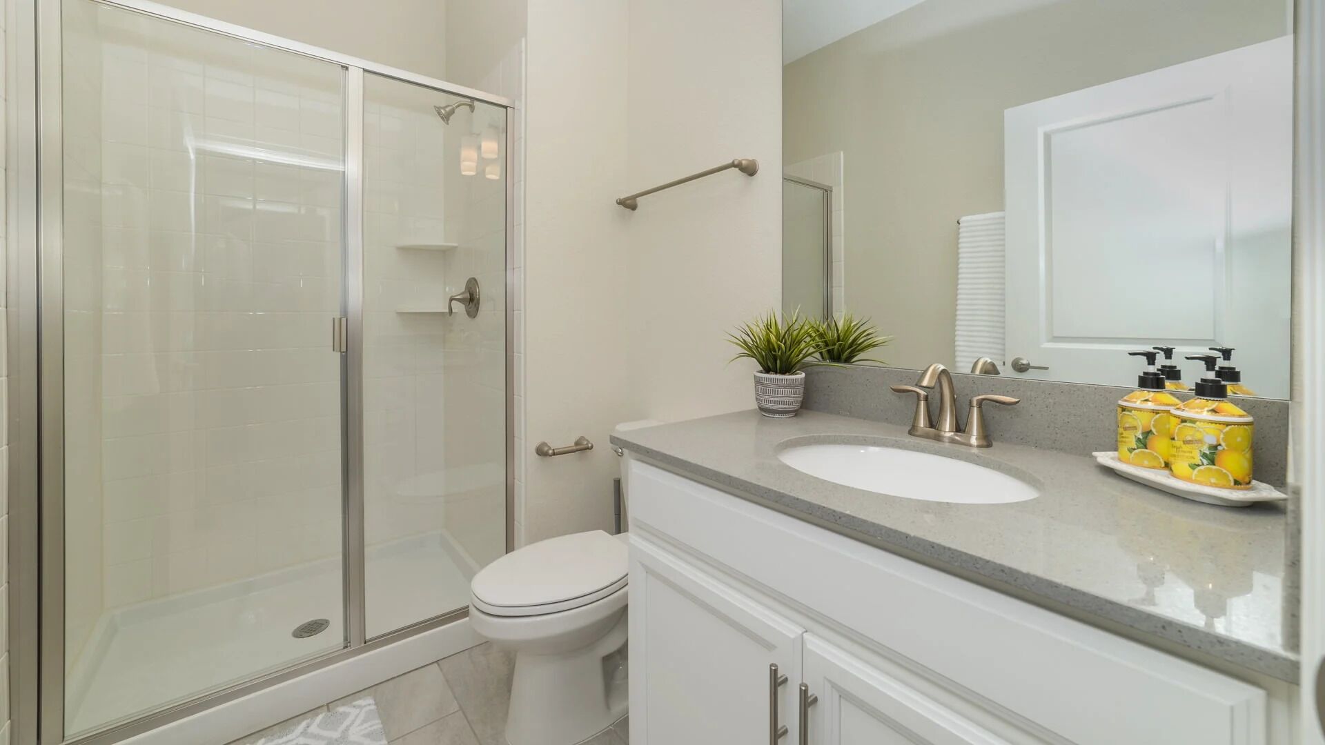 Une salle de bain moderne avec une douche à parois de verre, des toilettes blanches, un lavabo avec un miroir et des articles de toilette posés sur le comptoir.