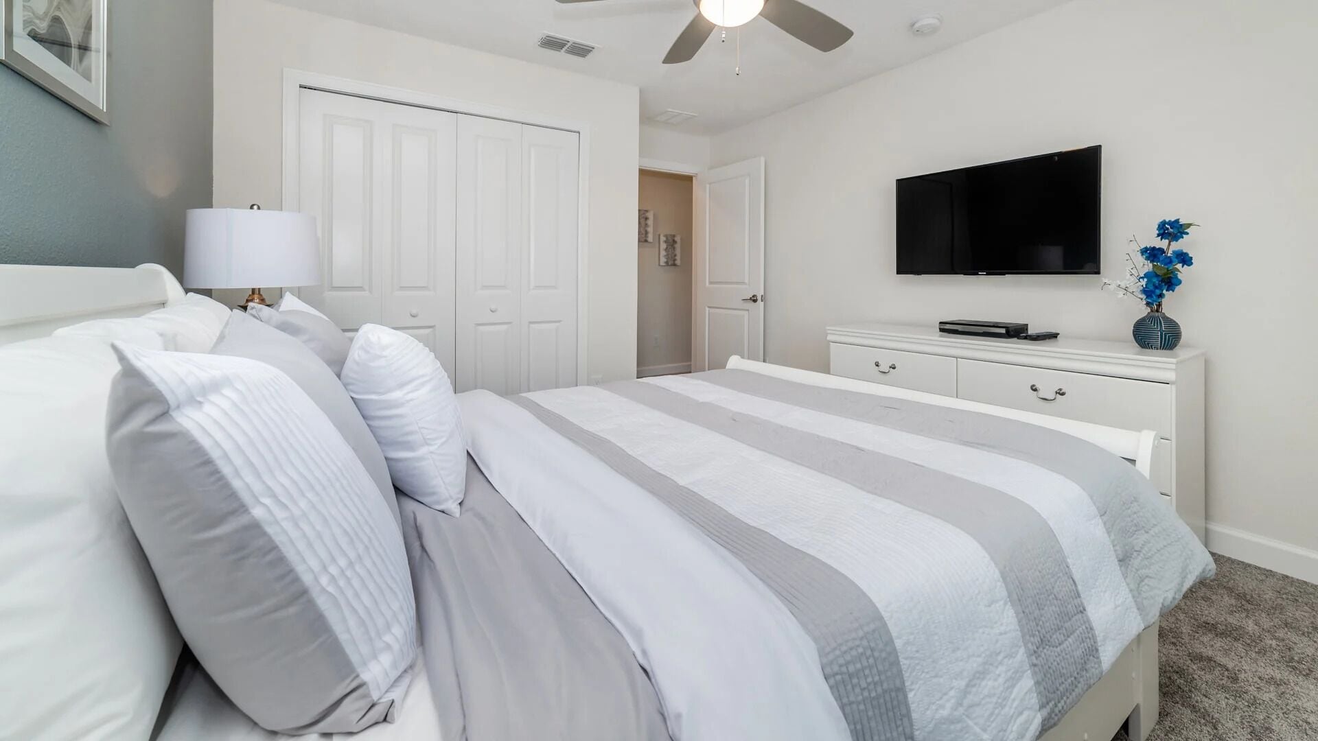 Een slaapkamer met een bed, een televisie, een dressoir en een plafondventilator.