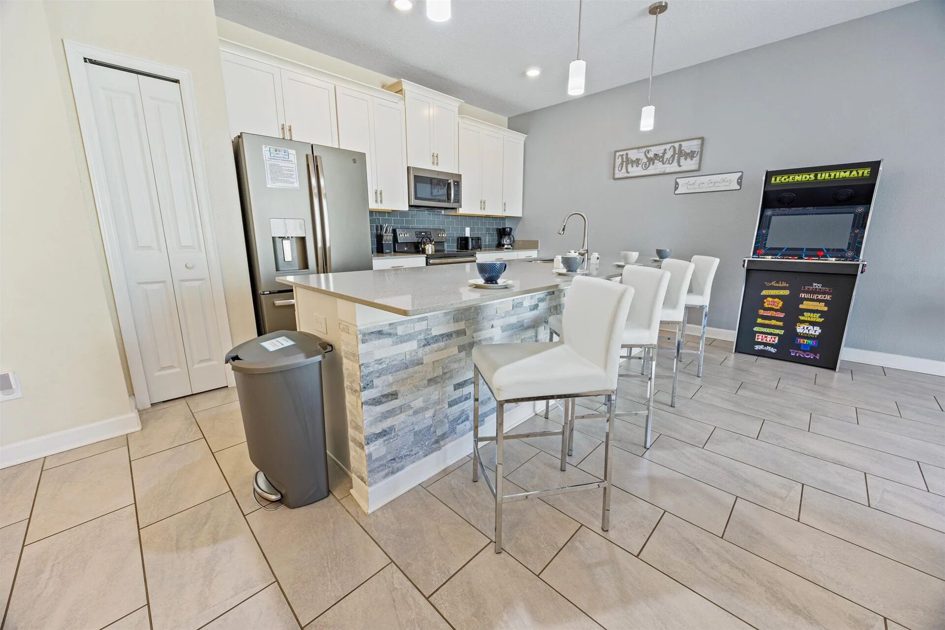 A modern kitchen with white cabinets, a granite island, and a bar area with white chairs.