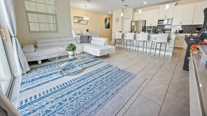 Ein modernes Wohnzimmer mit einem weißen Sofa, einem Glastisch und einem blauen Teppich mit Muster.