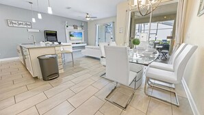 Eine moderne Küche mit Einbauofen, ein Essbereich mit Glastisch und weißen Stühlen sowie ein Deckenventilator.