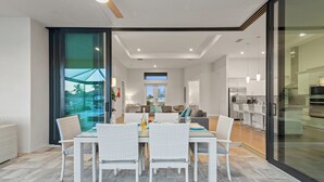 A modern kitchen with stainless steel appliances, a dining area with white wicker furniture, and a large sliding glass door leading to a balcony. - Intervillas Florida - Villa Cayman (Cape Coral)