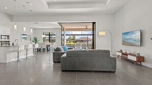 A modern living room with a grey sofa, a dining area with a white table, and a kitchen with white cabinets. - Intervillas Florida - Villa Cayman (Cape Coral)