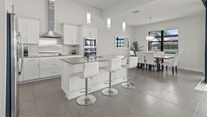 A modern kitchen with white cabinets, stainless steel appliances, and a central island with bar stools. - Intervillas Florida - Villa Cayman (Cape Coral)