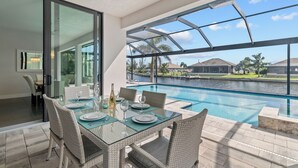 A dining area with a glass table and wicker chairs overlooking a swimming pool and a marina. - Intervillas Florida - Villa Cayman (Cape Coral)
