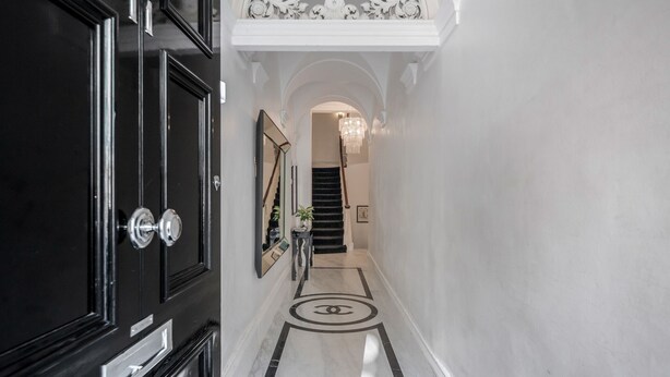 Um corredor com uma porta preta, um espelho, um candelabro e uma escadaria.