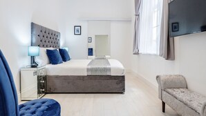 Quarto moderno com uma cama grande, mesas de cabeceira, uma televisão e um banco.