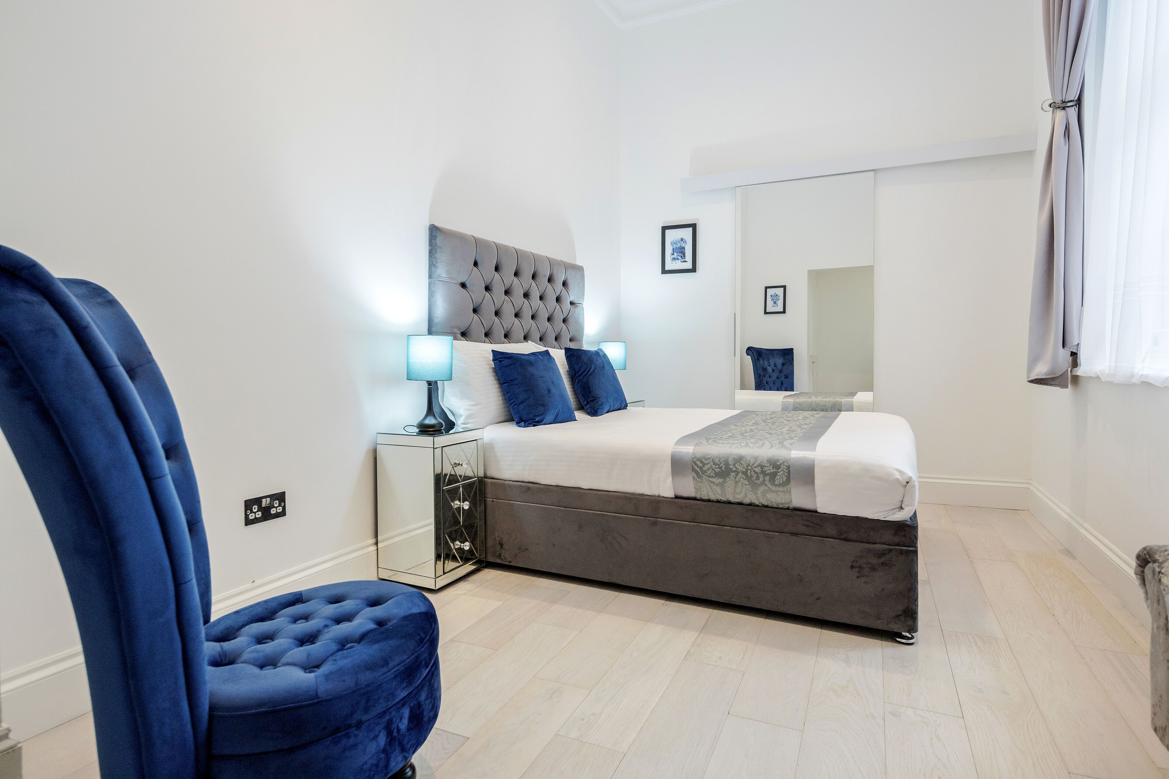 Une chambre à coucher moderne avec un grand lit, une tête de lit capitonnée, une table de chevet avec des lampes et un miroir.