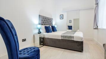 Une chambre à coucher moderne avec un grand lit, une tête de lit capitonnée, une table de chevet avec des lampes et un miroir.